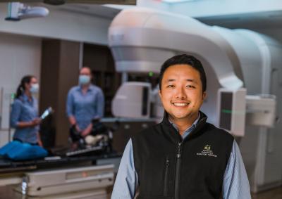 A radiation professional standing in front of a machine smiling.