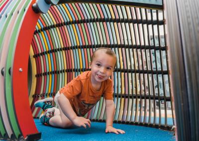 A young child crawling through play equipment at the hospital. The child has stitches in his forehead from an operation.