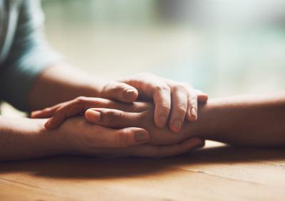 Two people holding hands over a table. One is supporting the other.