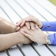 Two people sitting across from each other with their hands placed together in support of each other.